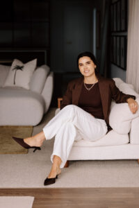 Professional woman in brown blazer sitting on cream sofa in modern bedroom